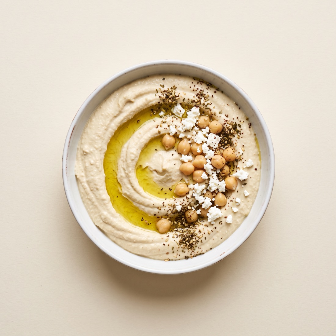 Tazón de dip cremoso claro con garbanzos, queso feta desmoronado y aceite de oliva, vista cenital