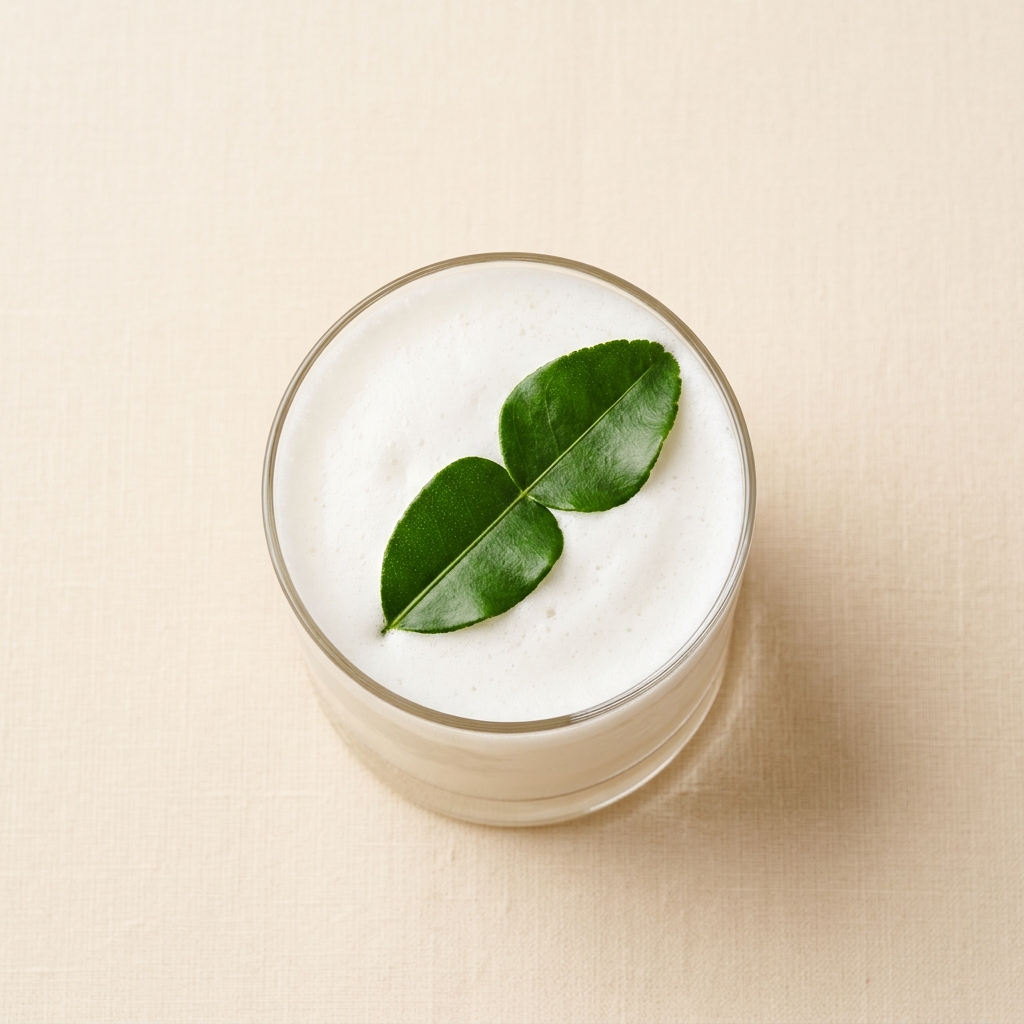 Coctel de mezcal y guanábana en vaso corto con espuma de coco y hoja de kaffir, vista cenital