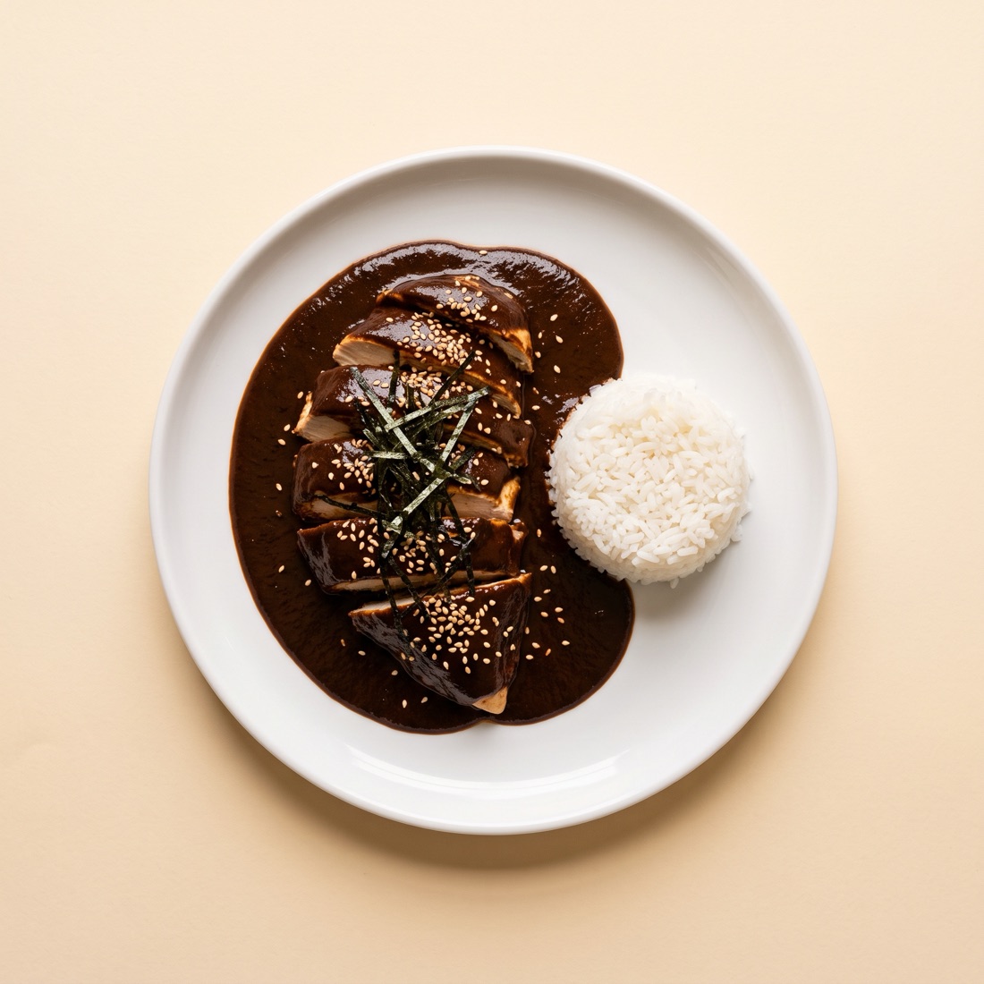 Pollo bañado en mole con ajonjolí y tiras de nori, con arroz blanco, sobre un plato blanco, vista cenital